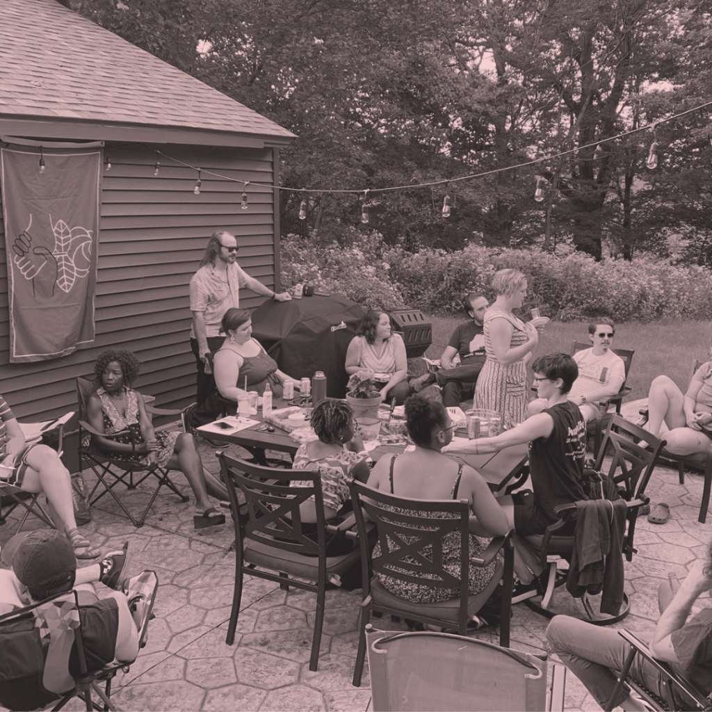A light red and black filter with people sitting around on an outdoor patio and conversing. A DSA flag hangs from the wall of a building in the background.